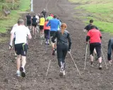 Grupp som går uppför en lerig backe med stavar, en aktivitet som liknar nordic walking.