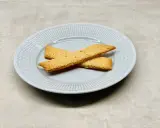 Två gyllene kolasnittar ligger korslagda på en ljusblå tallrik. Perfekt för ett enkelt kolasnittar recept.