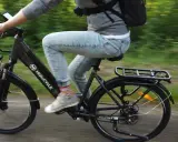 Osoba na rowerze Molicyle, który wygląda jak rower miejski czy trekkingowy, jedzie po ścieżce wśród zieleni.