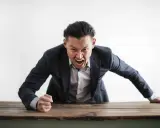 Wütender Mann im Anzug schreit über einen Tisch. Darf ein Lehrer Schüler anschreien?