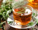 Une tasse de tisane romarin, avec des brins de romarin frais sur la soucoupe et en arrière-plan.