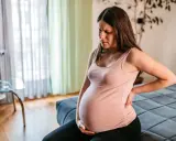 Schwangere Frau im 3. Trimester mit oberbauchschmerzen, hält sich den Rücken.