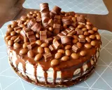 Pyszny tort kinder bueno, obficie udekorowany kawałkami batoników i czekoladowymi drażetkami, spływający karmelem.
