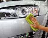 Dłoń z zieloną mikrofibrą poleruje błyszczący lakier srebrnego samochodu, podkreślając perfekcyjny auto detailing.