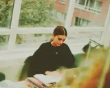 Studentka pochłonięta nauką kryminologii w Poznaniu, siedzi przy oknie z laptopem i książkami.