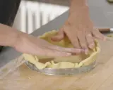 Mains expertes pour foncer une pâte dans un cercle à tarte. La pâte est étalée et ajustée sur les bords.