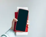 Dłoń trzyma iPhone'a w czerwonym etui. Czy iPhone jest bezpieczny? Zależy od użytkownika i jego nawyków.