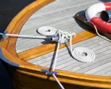Détail d'une peinture de bateau en bois, avec cordages blancs et une bouée de sauvetage rouge et blanche.