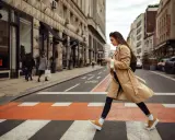 Kobieta w beżowym płaszczu i żółtych sneakersach przechodzi przez pasy. Idealne buty do trencza na miejski spacer.