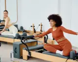 Dwie kobiety ćwiczą na reformerach. To świetny sposób, by dowiedzieć się, pilates co to jest i jak poprawić kondycję.