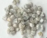 Un mucchio di grezzi diamanti non lavorati, con sfumature che vanno dal bianco al grigio e un leggero tocco dorato, pronti per essere trasformati.