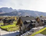 Nowoczesne domki na odludziu w górach, otoczone jesienną przyrodą i majestatycznymi szczytami.