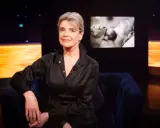 Stina Ekblad sitter i en mörkblå soffa, med en skärm bakom sig som visar klipp från filmer och tv-program med henne.