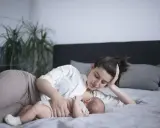 Mama karmi na leżąco swoje dziecko na łóżku. Czuły moment bliskości i spokoju.