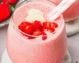 Un délicieux smoothie fraise banane, garni de morceaux de fruits frais et de pailles rayées roses et blanches.