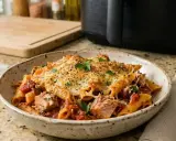 Un plato de macarrones con atún gratinados, con trozos de pescado y salsa de tomate, decorado con perejil fresco.