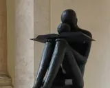 Statua di una figura che legge un libro, con un bambino appoggiato. Un'immagine che evoca il "sursum corda traduzione" della conoscenza.