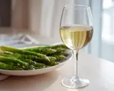 En tallrik med färsk grön sparris bredvid ett glas vitt vin. Perfekt kombination för en lätt och fräsch måltid.