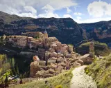 Malerisches Dorf Albarracín, Spanien, schmiegt sich an steile Felsen. Ein Weg führt durch grüne Hügel zum historischen Ortskern.