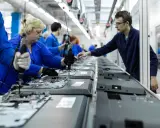 Pracownicy w niebieskich kombinezonach montują telewizory na linii produkcyjnej. To praca w ruchu ciągłym, gdzie każdy element jest kluczowy.