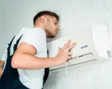 Técnico realiza mantenimiento preventivo de aire acondicionado, ajustando la unidad con un destornillador.