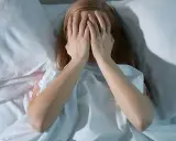 Nastolatka w łóżku, zakrywająca twarz dłońmi, symbolizuje bezsenność u nastolatków i jej przyczyny.