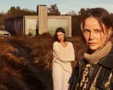 Två kvinnor står i ett torrt landskap framför ett modernt hus. En polisbil syns i bakgrunden. Sanningen serie.