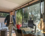 Un homme en costume entre dans un bureau lumineux avec vue sur un jardin. C'est la définition du home office : travailler depuis chez soi.