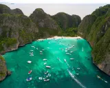 Maya Bay tętni życiem, pełna łodzi i turystów na piaszczystej plaży, otoczona stromymi, porośniętymi zielenią klifami.