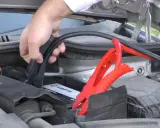 Mano conectando pinzas rojas a la batería de un coche para arrancar con pinzas.