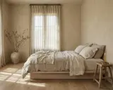 Camera da letto con pareti color sabbia, letto con biancheria in lino beige, vaso con rami secchi e candela. Ideale per capire quali pareti dipingere in una stanza.
