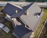 Nowy dach z ciemnej dachówki, z dwoma kominami i lukarną. Elewacja domu w odcieniach beżu i brązu. Facjata domu prezentuje się okazale.
