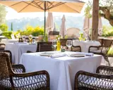 Tables dressées en terrasse, sous un parasol, invitant à savourer une cuisine du terroir authentique. Vins, verres et couverts attendent les convives.