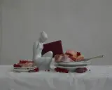 A white porcelain figure contemplates raw meat and red currants, a scene reminiscent of Evelyn Bencicova's still lifes.