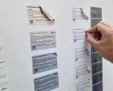 Ręka zrywa etykietę z folii, która jest surowcem dla drukarni. Widać różne rodzaje folii, m.in. srebrną matową i białą błyszczącą.