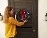 Dziewczyna w żółtym swetrze wiesza świąteczny wieniec na drzwiach. To świetny sposób, jak ozdobić drzwi na święta.