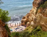 Sonnige Praia do Carvalho mit Felsen, grüner Vegetation und Badegästen am Meer.