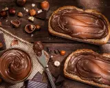 Selbstgemachte Haselnusscreme auf Brot, umgeben von Nüssen und Schokolade. Ein Genuss, der zum Nachmachen einlädt.