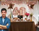 Mężczyzna w kratę stoi przed stołem z prezentami i balonami z napisem "Happy Birthday 40".