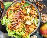 Ein bunter asiatischer Salat mit gegrilltem Hähnchen, Avocado, Mango, Karottenstreifen und Erdnüssen.
