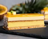 Un délice tropical : un entremets aux couches crémeuses, surmonté d'un glacage miroir jaune éclatant, décoré de fruits et de noix de coco râpées.