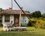 Kolorowy dom i studnia w malowniczej wsi Zalipie, ozdobione ludowymi wzorami kwiatowymi.