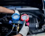 Manos enguantadas ajustan manómetros para saber como cargar aire acondicionado coche.