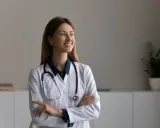 Une podologue souriante, avec un stéthoscope autour du cou, réfléchit à la rédaction d'une lettre pour le médecin traitant.