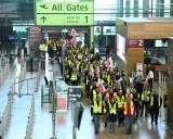 Tłum pracowników w kamizelkach odblaskowych z flagami maszeruje przez lotnisko w Berlinie, protestując. Strajk lotnisko Berlin zakłóca ruch.
