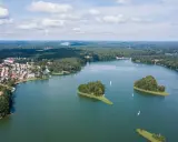 Malownicze jezioro w Polsce otoczone lasami, z wyspami i żaglówkami. Widok na miasteczko przy brzegu.