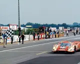 Ein roter Porsche Rennwagen mit der Startnummer 23 überquert die Ziellinie, während eine karierte Flagge geschwenkt wird.