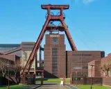 Industrielles Erbe mit rotem Förderturm und Backsteingebäuden. Die Zeche Zollverein strahlt eine starke, urbane Energie aus.