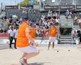 Joueur de pétanque concentré, cherchant à faire le vide dans sa tête avant de lancer la boule. Le public est installé dans les gradins derrière lui.