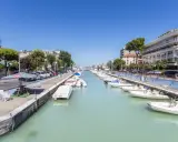 La darsena di Riccione, con barche ormeggiate lungo il canale, palazzi e alberi verdi sotto un cielo azzurro.